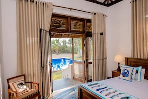 Ein Schlafzimmer mit einem Bett, einem Sessel, einem Nachttisch und Blick auf einen Außenpool.