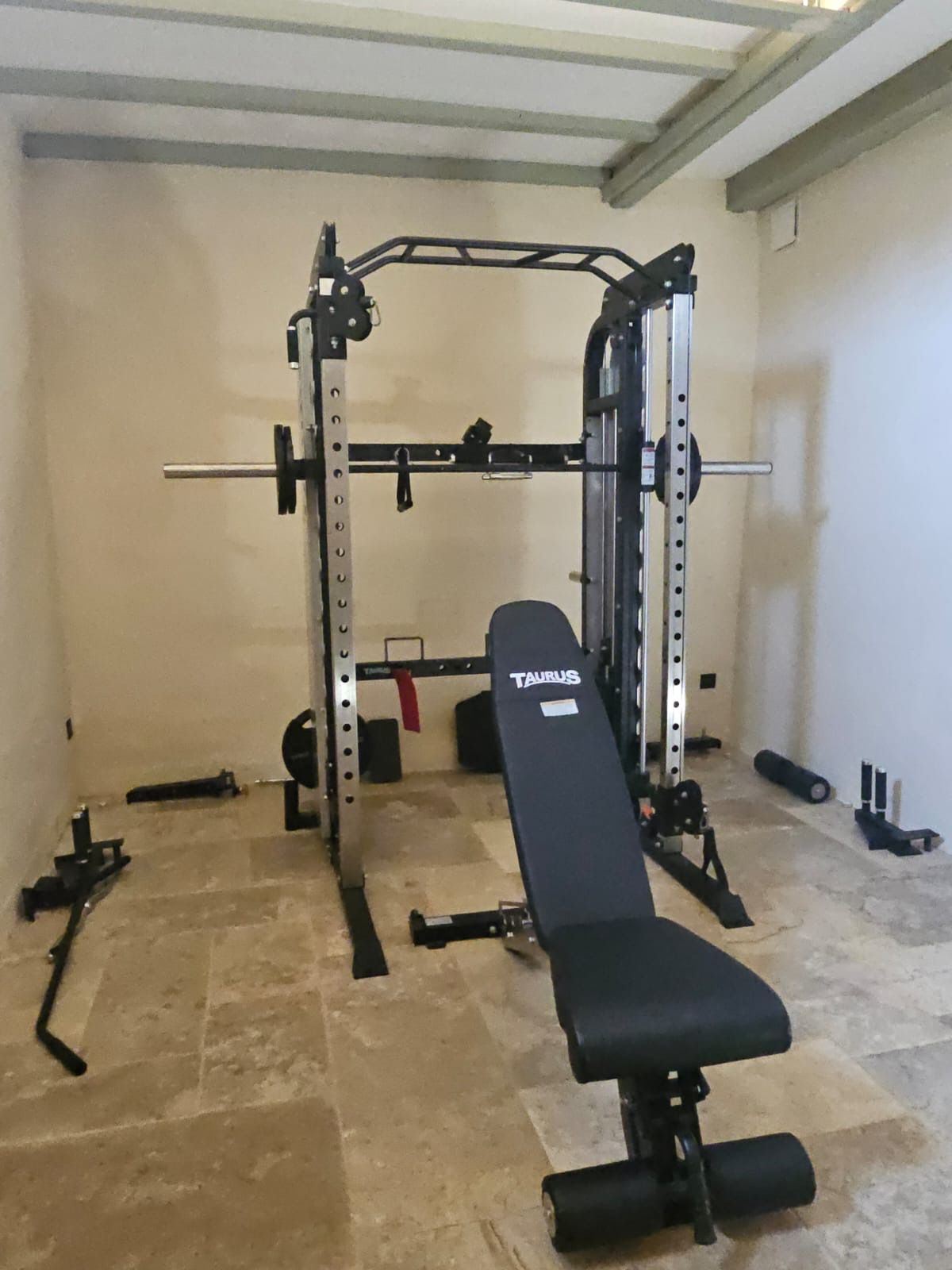 Une salle de sport équipée d’un banc de développé couché, d’un support à squats et de divers poids.