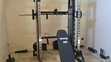 Une salle de sport équipée d’un banc de développé couché, d’un support à squats et de divers poids.