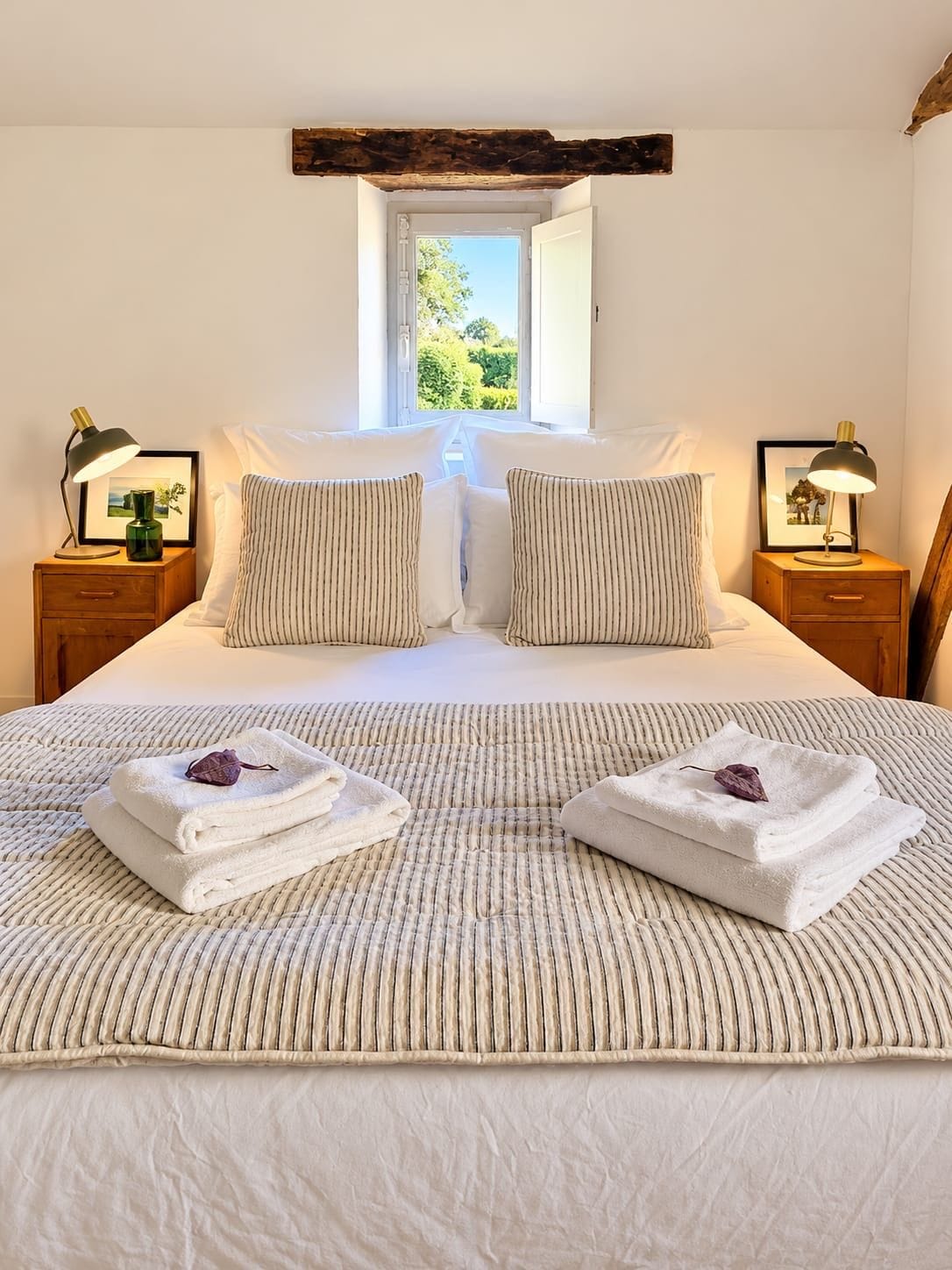 A neatly made bed with striped bedding, two pillows, and two bedside tables with lamps and framed pictures.