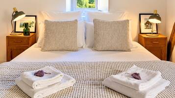 A neatly made bed with striped bedding, two pillows, and two bedside tables with lamps and framed pictures.