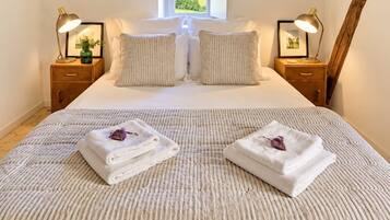 A bedroom with a large bed, two bedside tables with lamps, a window, and a wooden beam ceiling.