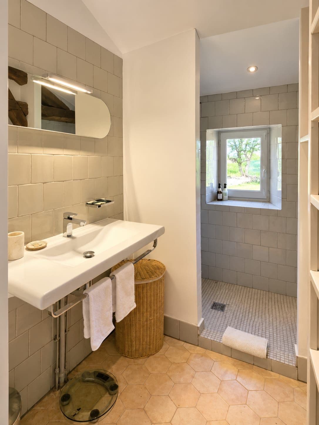 Une salle de bain moderne avec un lavabo blanc, un miroir et une douche séparée par une paroi vitrée.