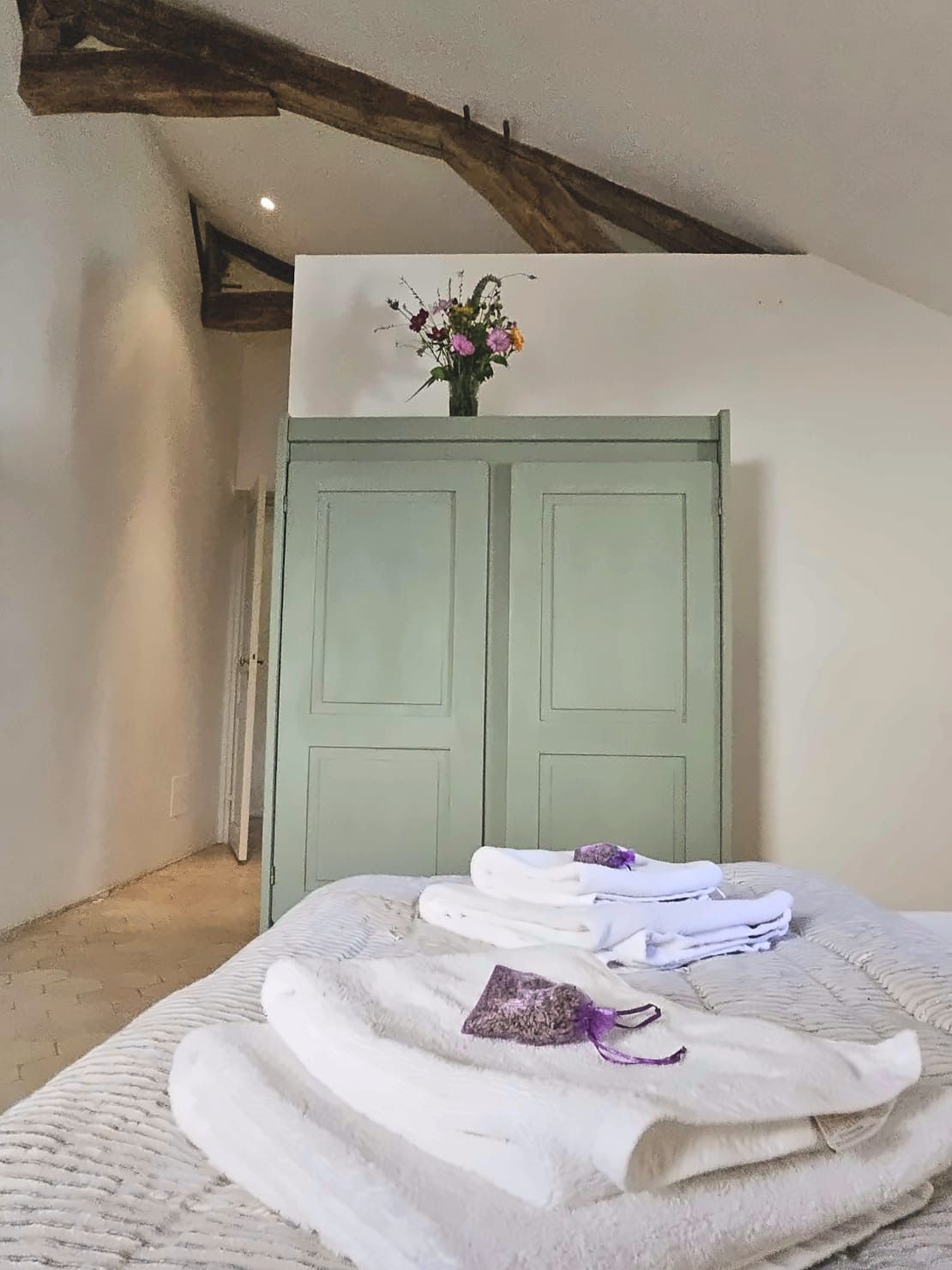 Une pièce avec un lit, une porte verte et un vase rempli de fleurs accroché au mur.