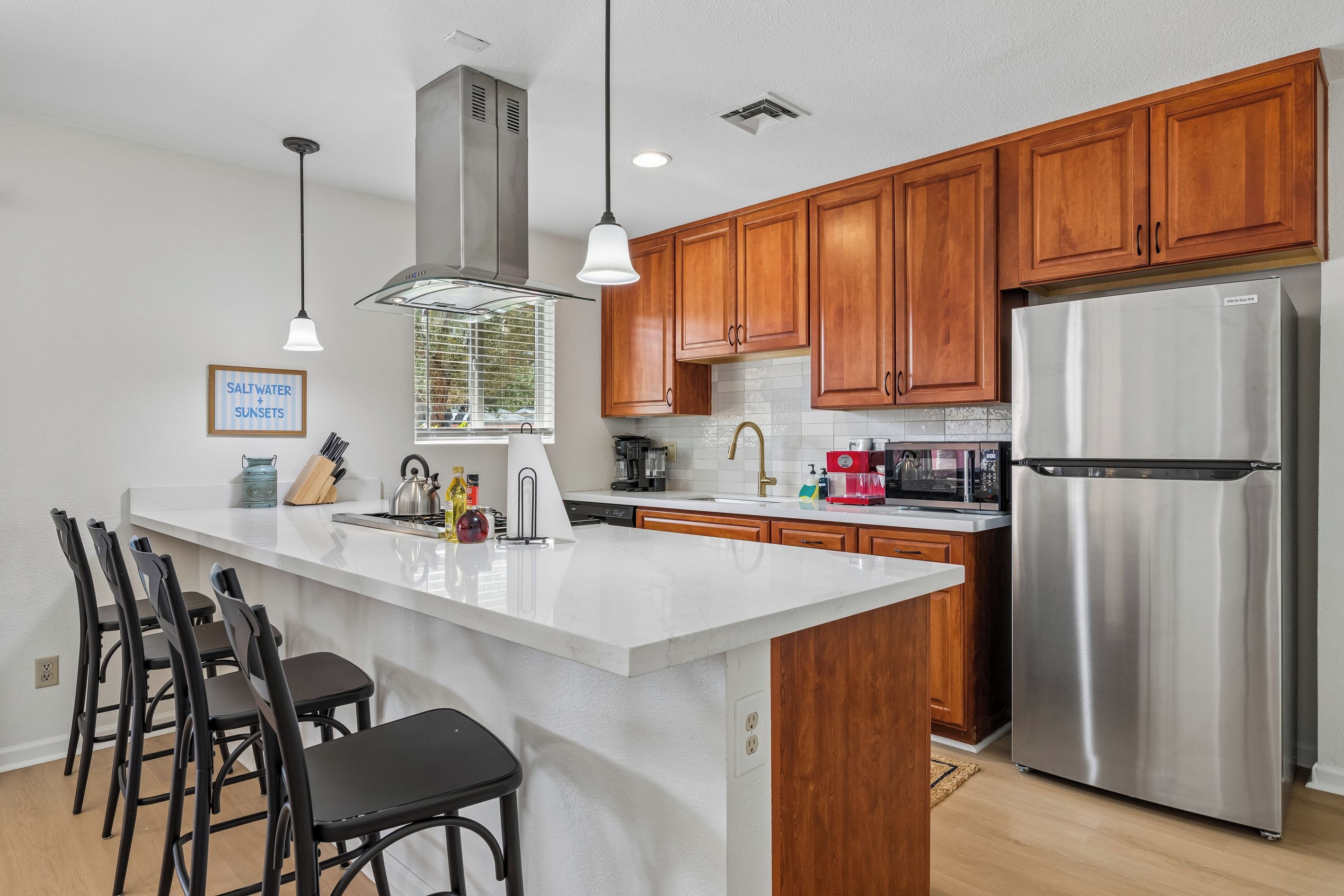 A modern kitchen with wooden cabinets, a stainless steel refrigerator, and a central island with bar stools.