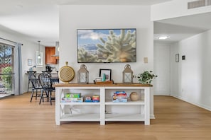 Un salon avec une console blanche, un téléviseur fixé au mur et une œuvre d’art représentant un cactus.