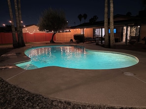 Une piscine à bordures courbes, entourée d’une terrasse en béton et d’une clôture en bois.