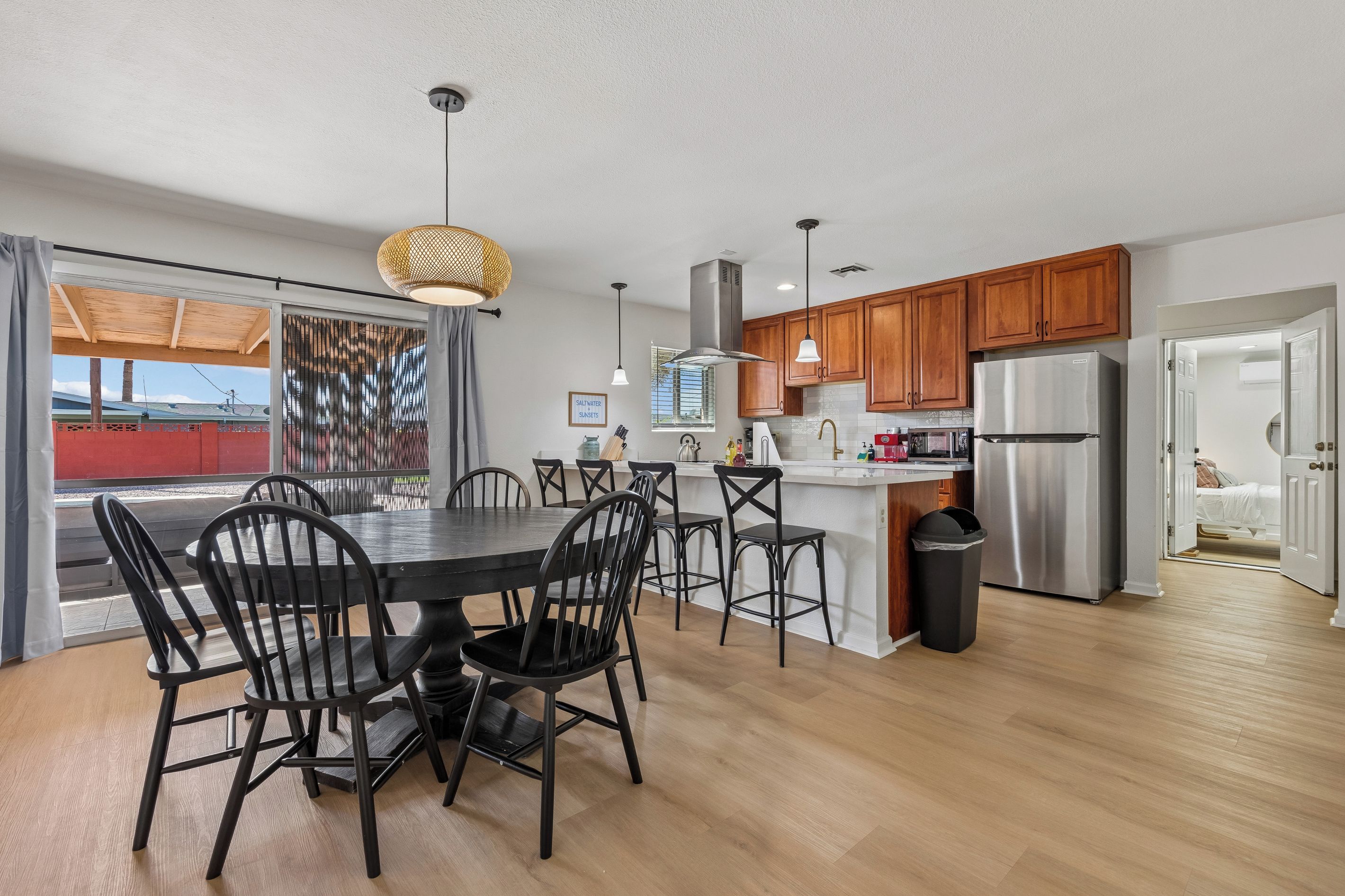 A modern kitchen with wooden cabinets, a stainless steel refrigerator, and a dining area with a round table and chairs.