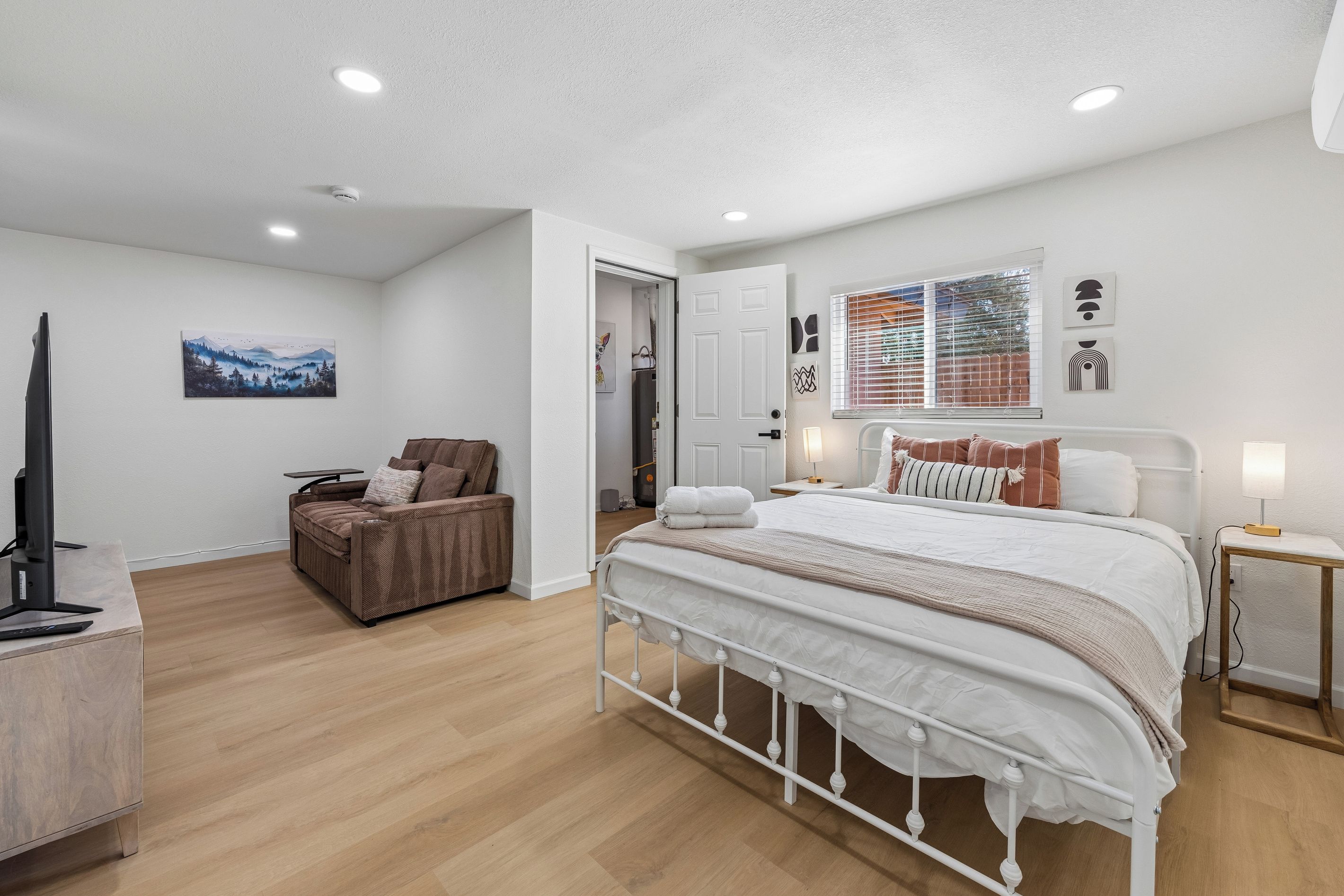 Une chambre moderne avec un grand lit, un coin salon avec un fauteuil, un téléviseur à écran plat et des œuvres d’art accrochées aux murs.