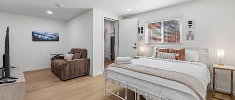 Une chambre moderne avec un grand lit, un coin salon avec un fauteuil, un téléviseur à écran plat et des œuvres d’art accrochées aux murs.
