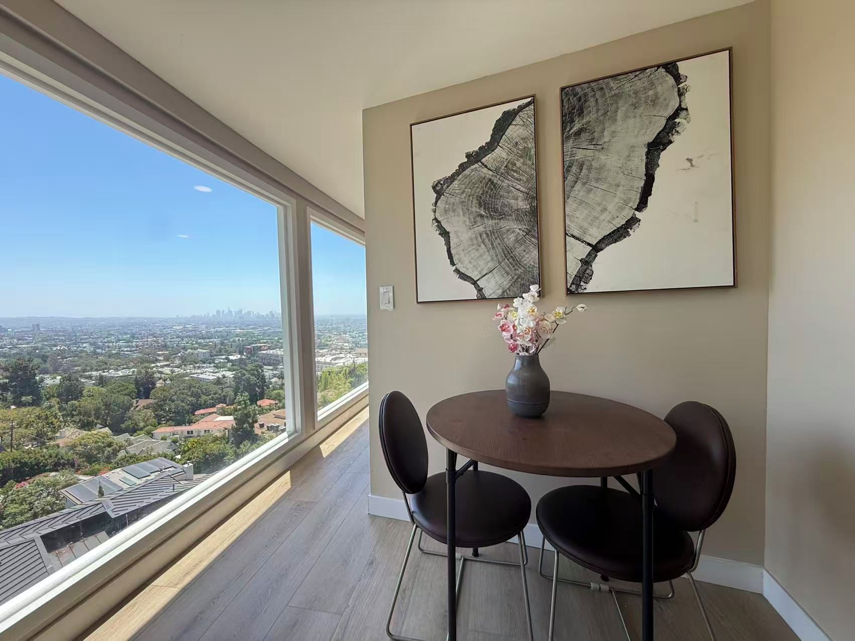 A dining area with a round table and four chairs, a vase with flowers, and two abstract paintings on the wall.