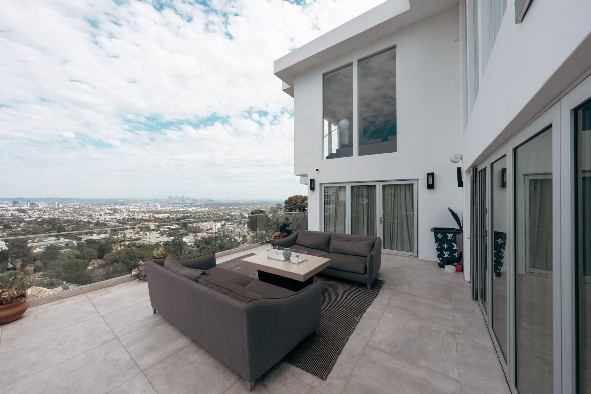 A modern outdoor living space with a sofa and coffee table, a view of the city, and a large window.