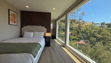 A bedroom with a large bed, a nightstand, a lamp, and a view of a hilly landscape.