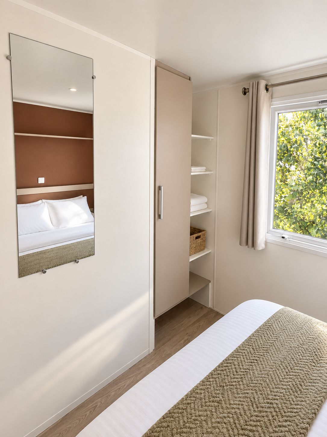 Ein Schlafzimmer mit einem Bett, einem Kleiderschrank, einem Spiegel und einem Fenster mit Vorhängen.