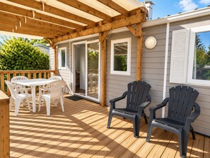 Una terraza de madera con un porche cubierto, sillas de plástico blanco y dos sillas tipo Adirondack.
