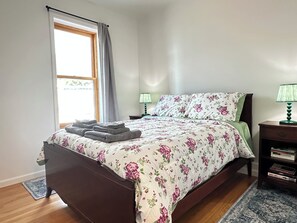 A bedroom with a bed, a nightstand, a lamp, and a window with curtains.