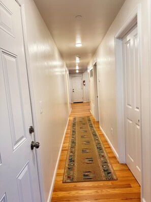 A hallway with white doors, a wooden floor, and a patterned rug.