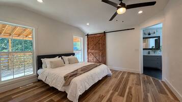 Un dormitorio con cama, suelo de madera, ventilador de techo y vistas al exterior.