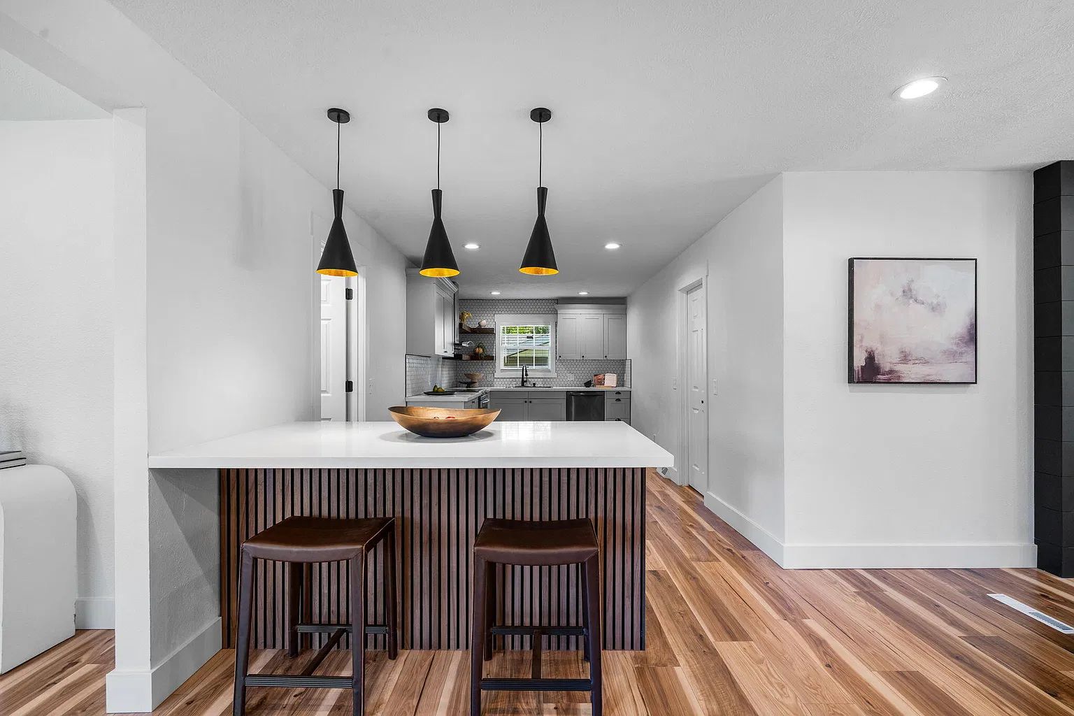A modern kitchen with a central island, pendant lighting, and a bar stool seating area.