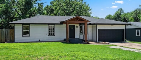 Ein eingeschossiges Haus mit Veranda, Garage und gepflegtem Rasen.