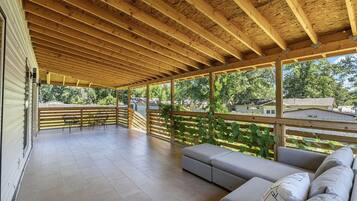 A covered outdoor patio with a wooden ceiling, a seating area with cushions, and a view of the surrounding neighborhood.