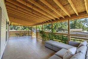 A covered outdoor patio with a wooden ceiling, a seating area with cushions, and a view of the surrounding neighborhood. - 4BR, 2 Suites & Covered Deck, Edge Of Springfield (Ozark)
