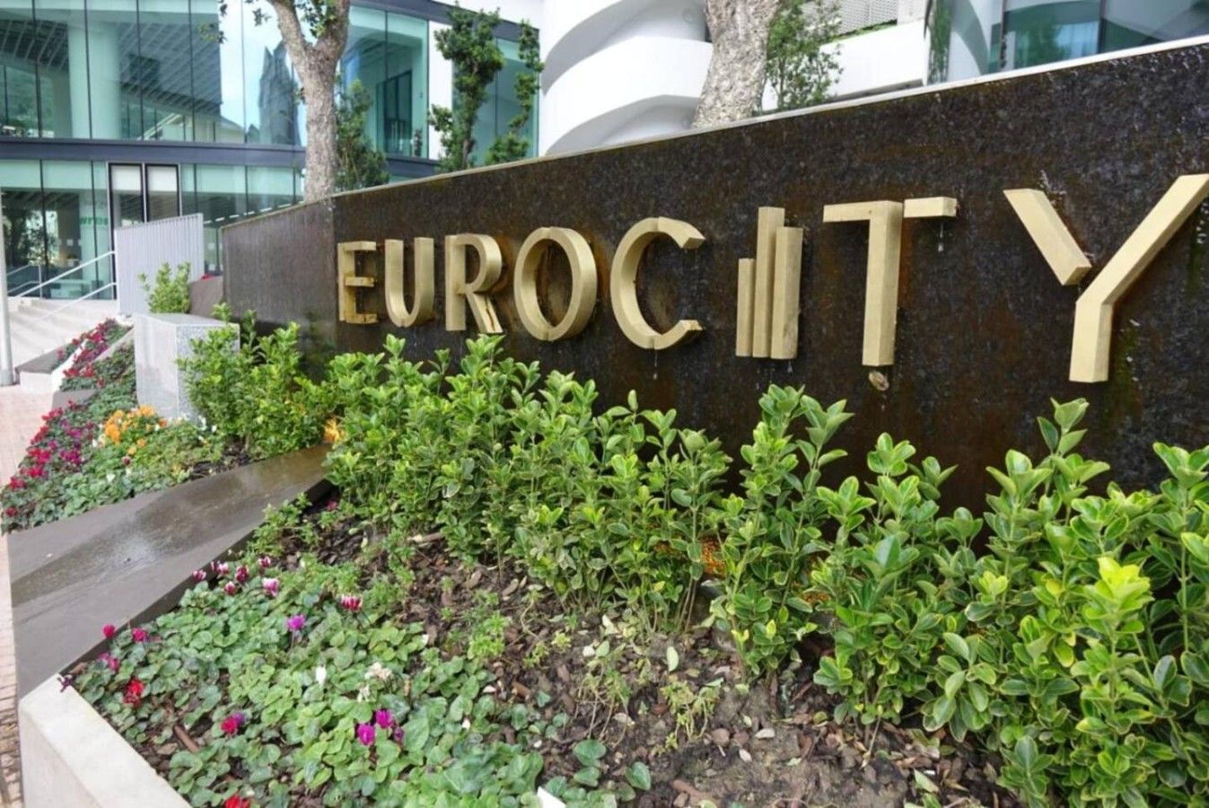 A sign with the words 'EUROCITY' in large letters, surrounded by a landscaped garden with various plants and flowers.