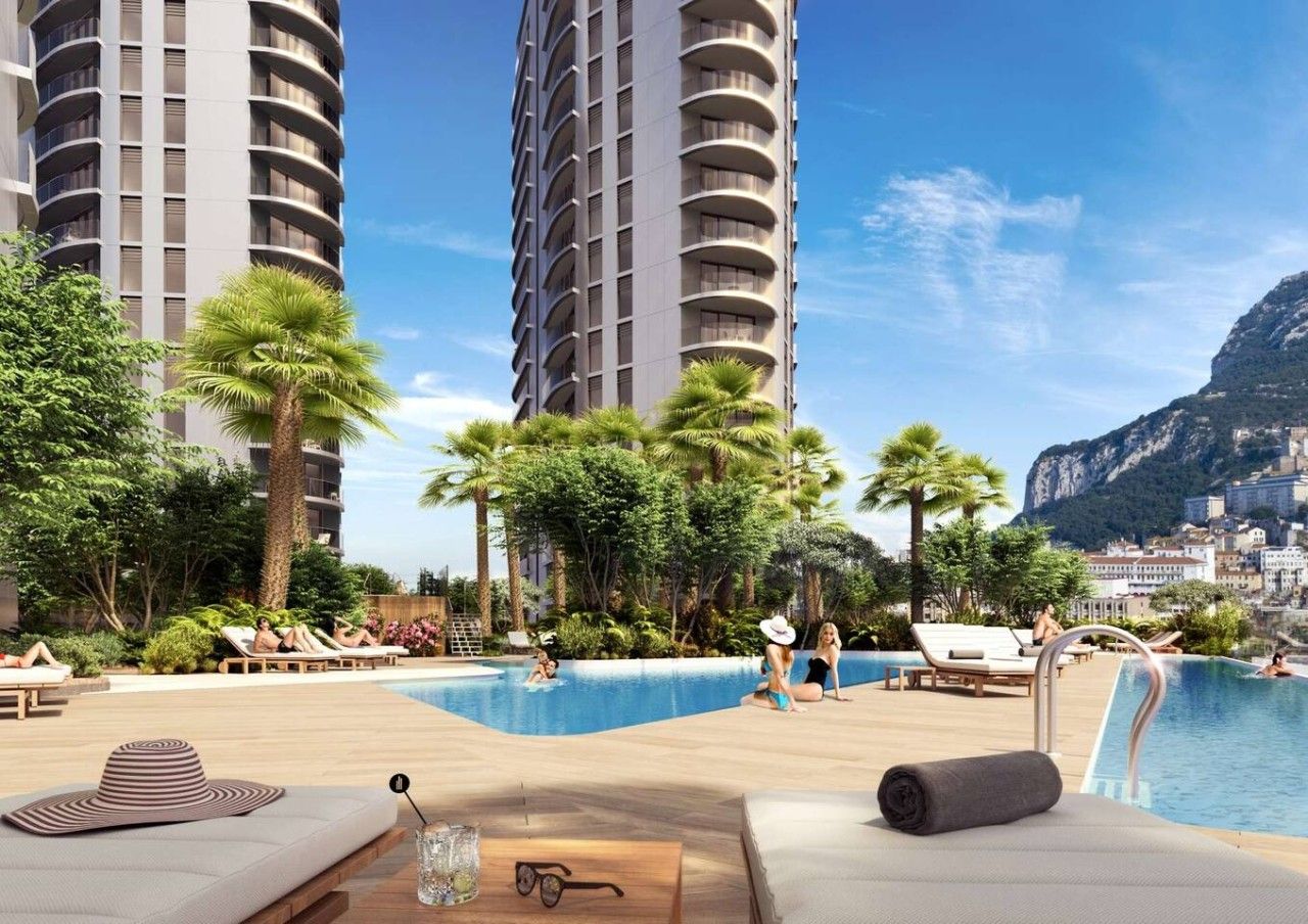 A poolside area with lounge chairs, a pool, and a view of tall buildings and a mountain.