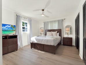 A bedroom with a bed, a ceiling fan, a TV, and a window with curtains. - Casa Selva (Orlando)