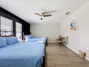 Una habitación de hotel con dos camas, un ventilador de techo, una mesita con sillas y un cuadro en la pared.