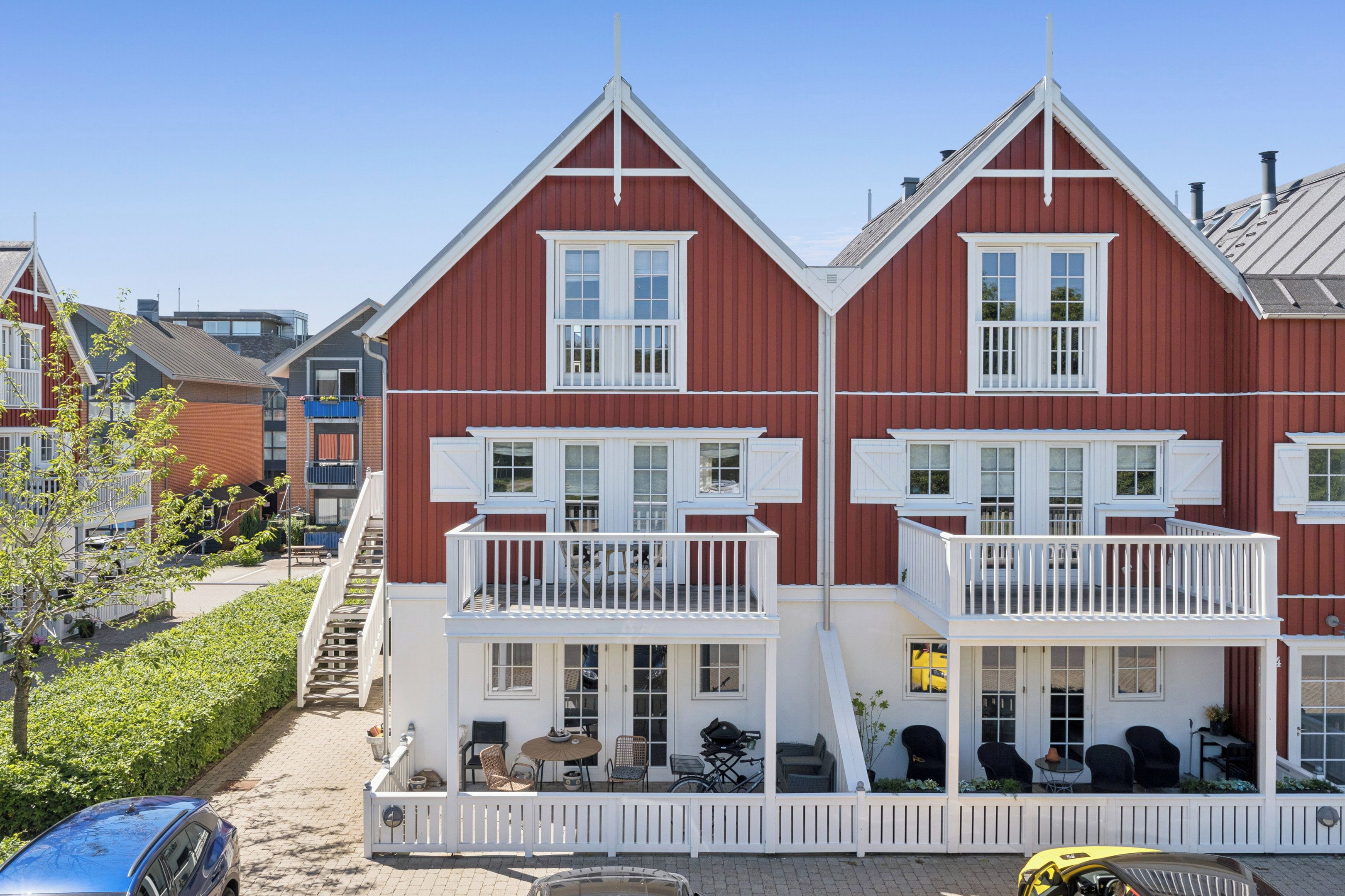 Un bâtiment rouge avec des ornements blancs, un balcon et un petit espace extérieur aménagé pour s’asseoir.