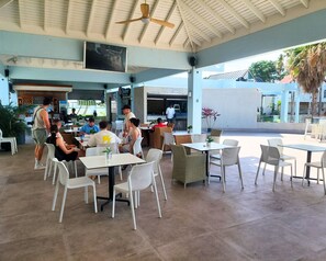 An outdoor cafe with tables and chairs, a ceiling fan, and a bar area. - Solara Boho West End Negril Stay (Negril)