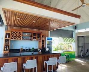A bar area with a counter, bar stools, a beverage dispenser, and a green ice cream cart. - Solara Boho West End Negril Stay (Negril)