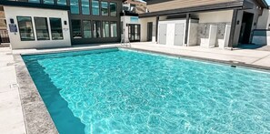 Ein Schwimmbecken mit klarem Wasser, neben einem Gebäude mit großen Fenstern und einem überdachten Bereich mit Schließfächern.