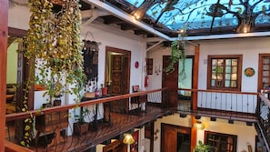 Un interno su più livelli con un balcone, ringhiere in legno e piante pendenti.