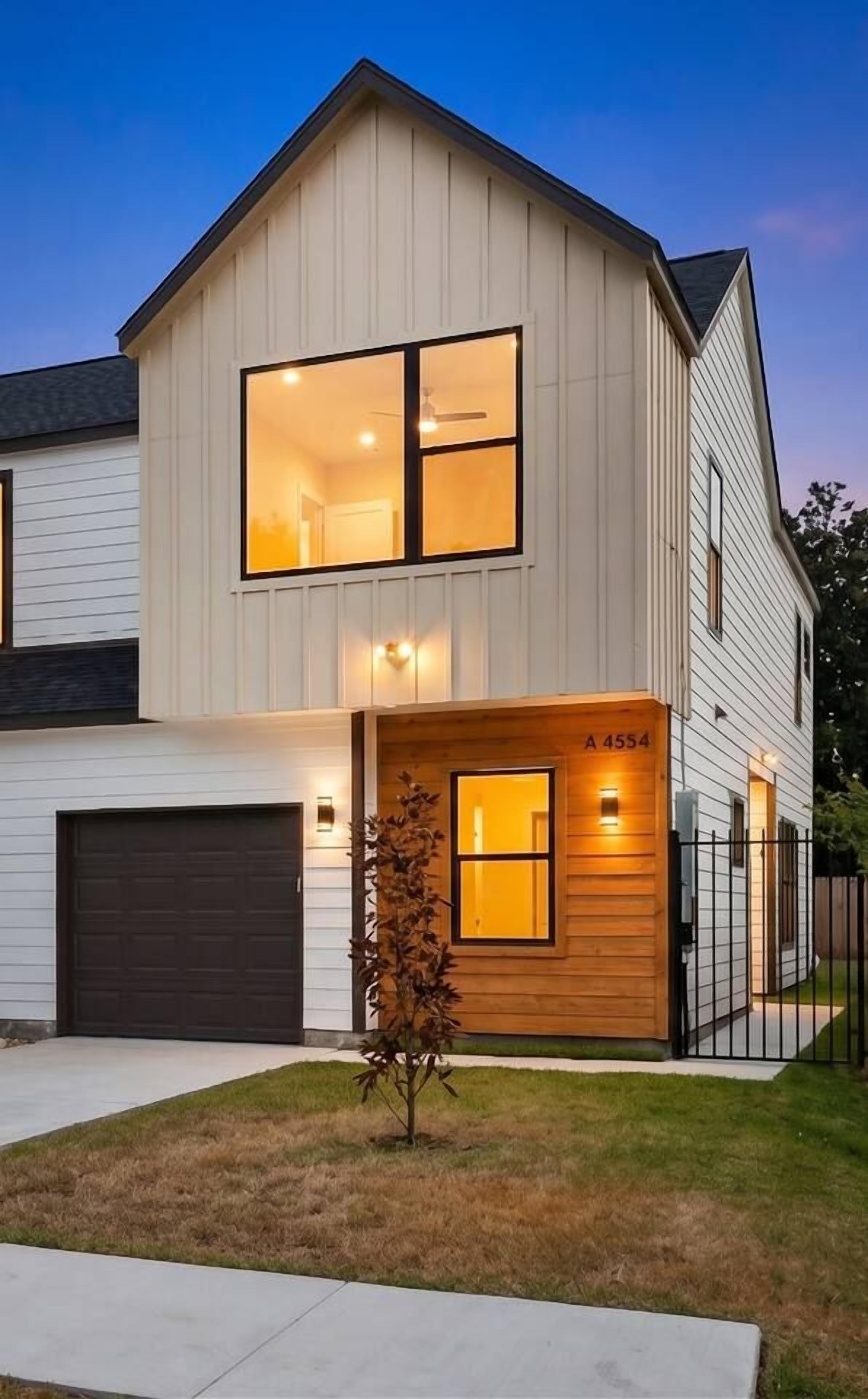 A modern two-story house with a garage, a wooden front porch, and a well-lit entrance.