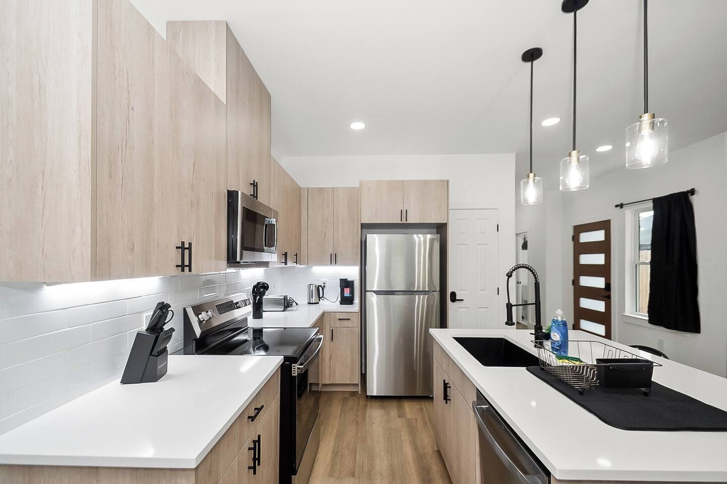 A modern kitchen with stainless steel appliances, white countertops, and wooden cabinetry.