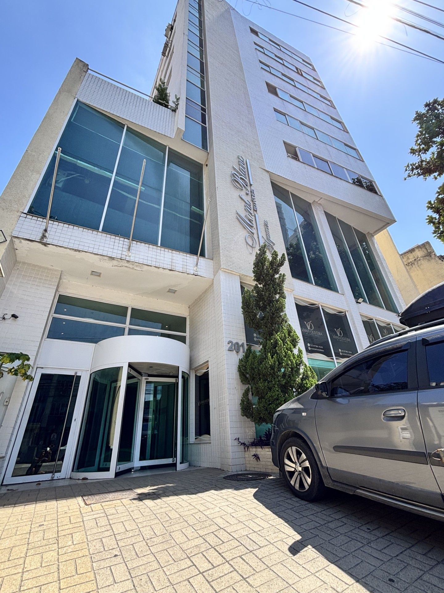 A modern building with a glass facade, a revolving door entrance, and a parked car in front.