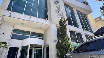A modern building with a glass facade, a revolving door entrance, and a parked car in front.