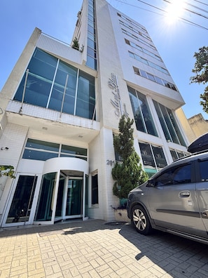 A modern building with a glass facade, a revolving door entrance, and a parked car in front.
