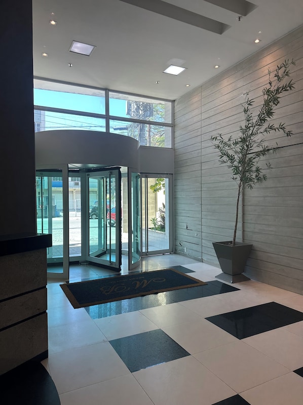 A lobby with a revolving door, a potted plant, and a checkered floor.