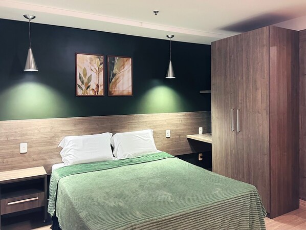 A bedroom with a bed, two bedside tables, a nightstand, a wardrobe, and two pendant lights.