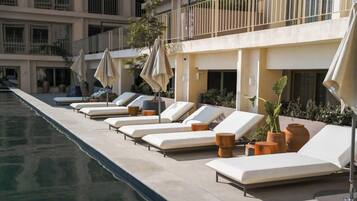 A poolside area with sun loungers and umbrellas, a clear pool, and a building with balconies.