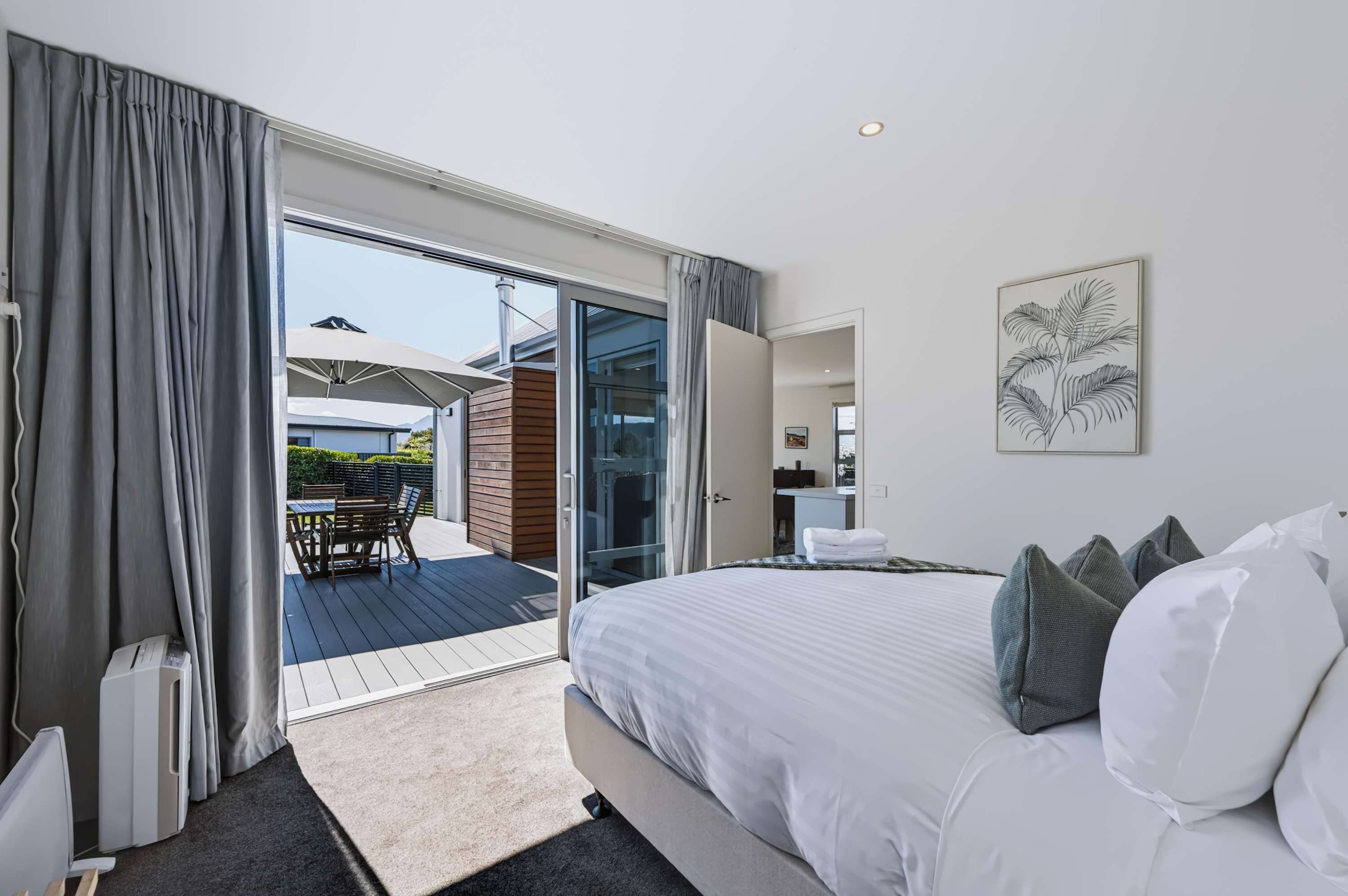 A modern bedroom with a large bed, a view of the outdoor patio, and a dining area.