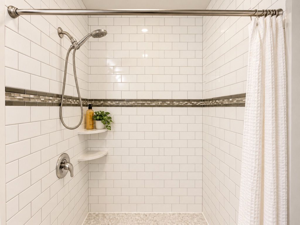 Un angolo doccia con pareti piastrellate di bianco, un soffione, un porta asciugamani e uno scaffale con articoli da toilette.