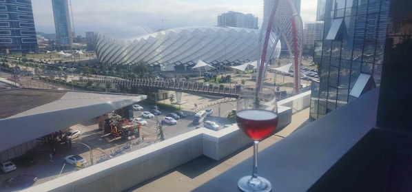 A modern building with a unique curved roof, a parking area, and a glass structure reflecting the cityscape. - Cozy Apartment for Rent in Batumi! Stadium View (Batumi)