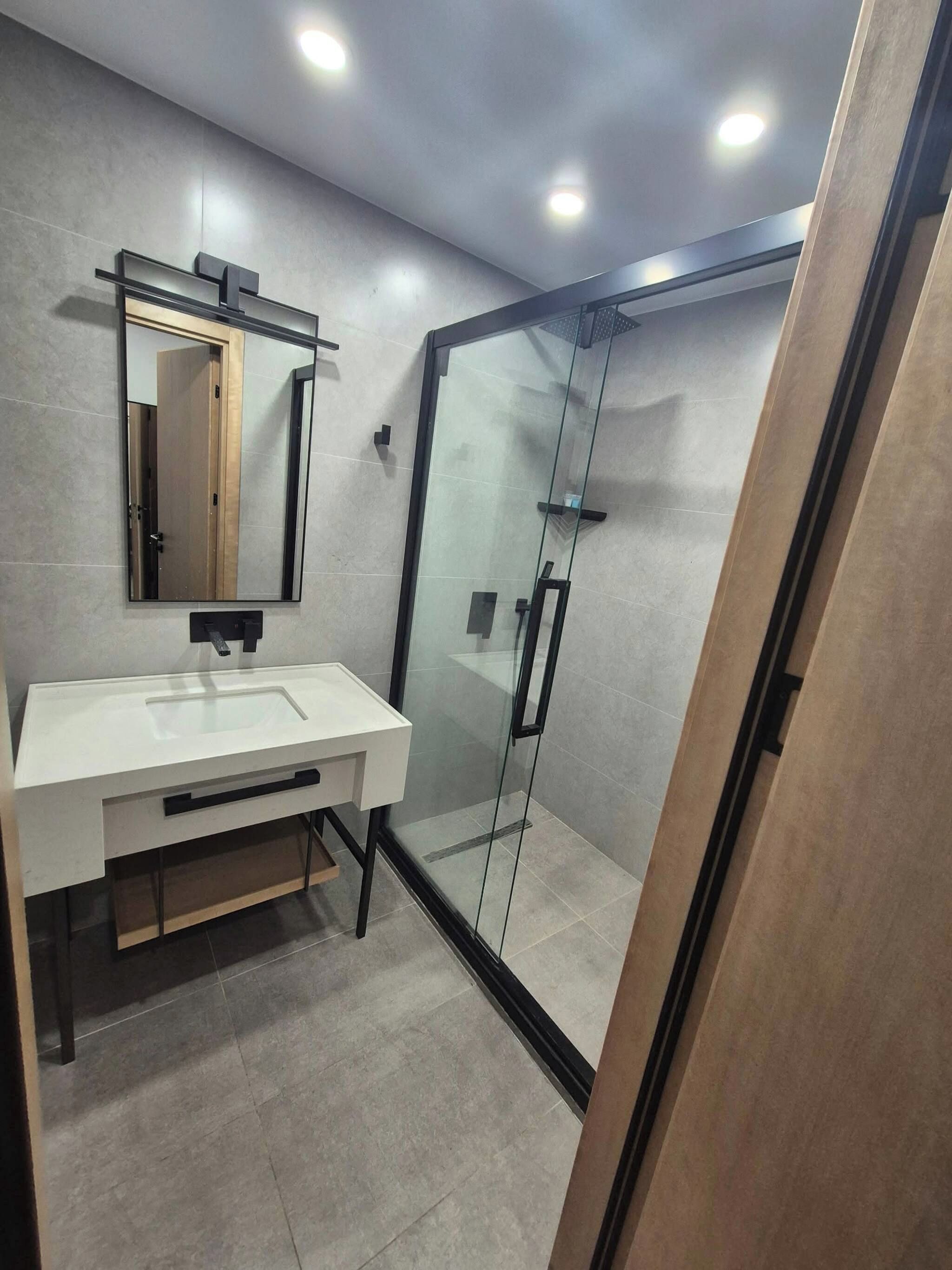 Un baño moderno con ducha envuelta en vidrio, un lavabo blanco y un espejo sobre él.