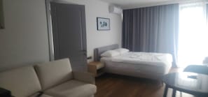A hotel room with a bed, a sofa, a small table, and a door. - Cozy Apartment for Rent in Batumi! Stadium View (Batumi)