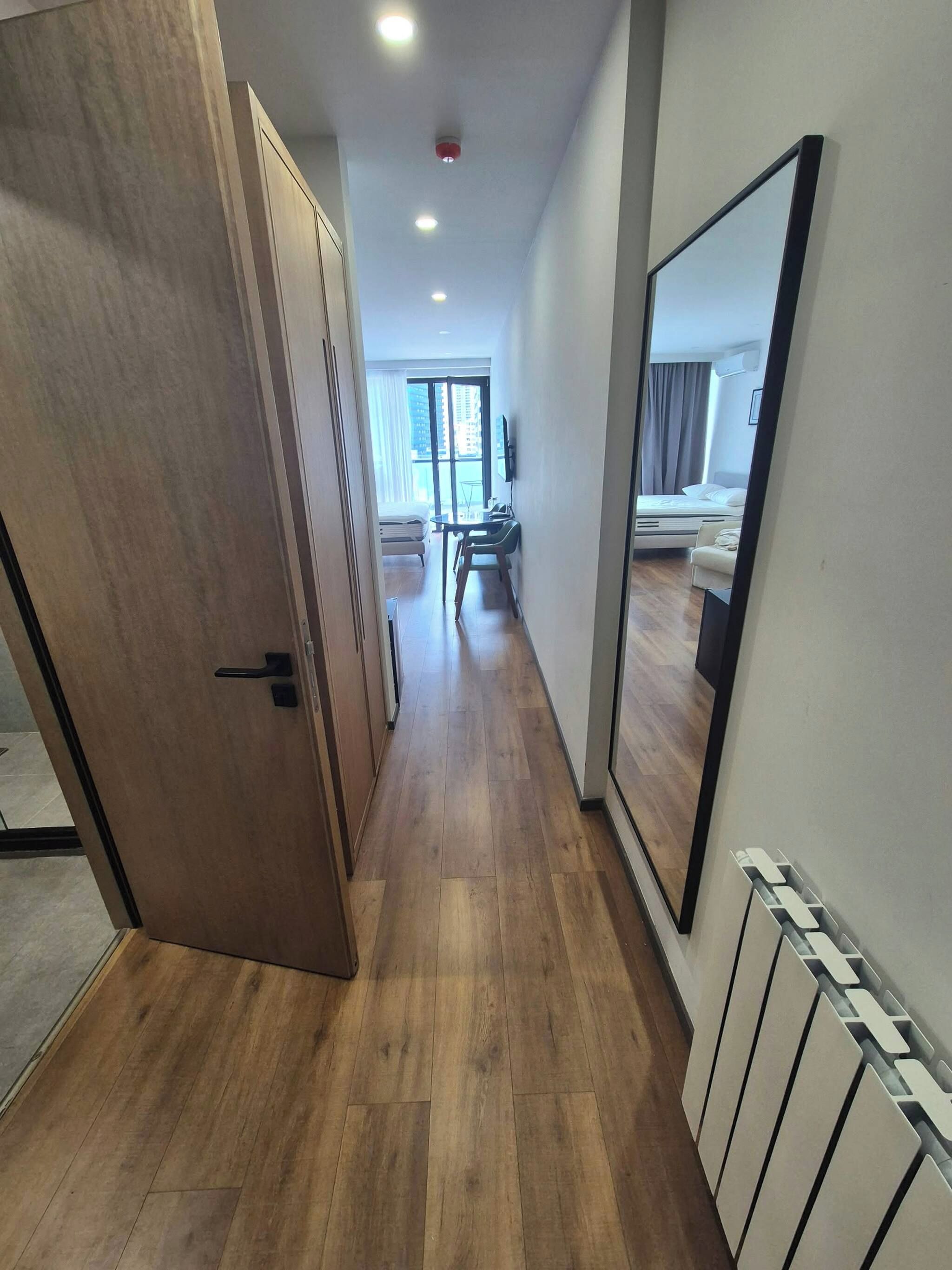 Un pasillo con suelo de madera, una puerta a la izquierda y un espejo grande a la derecha.