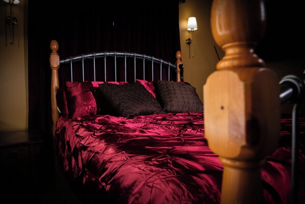 A bed with a headboard, red bedding, and two wall-mounted lamps.